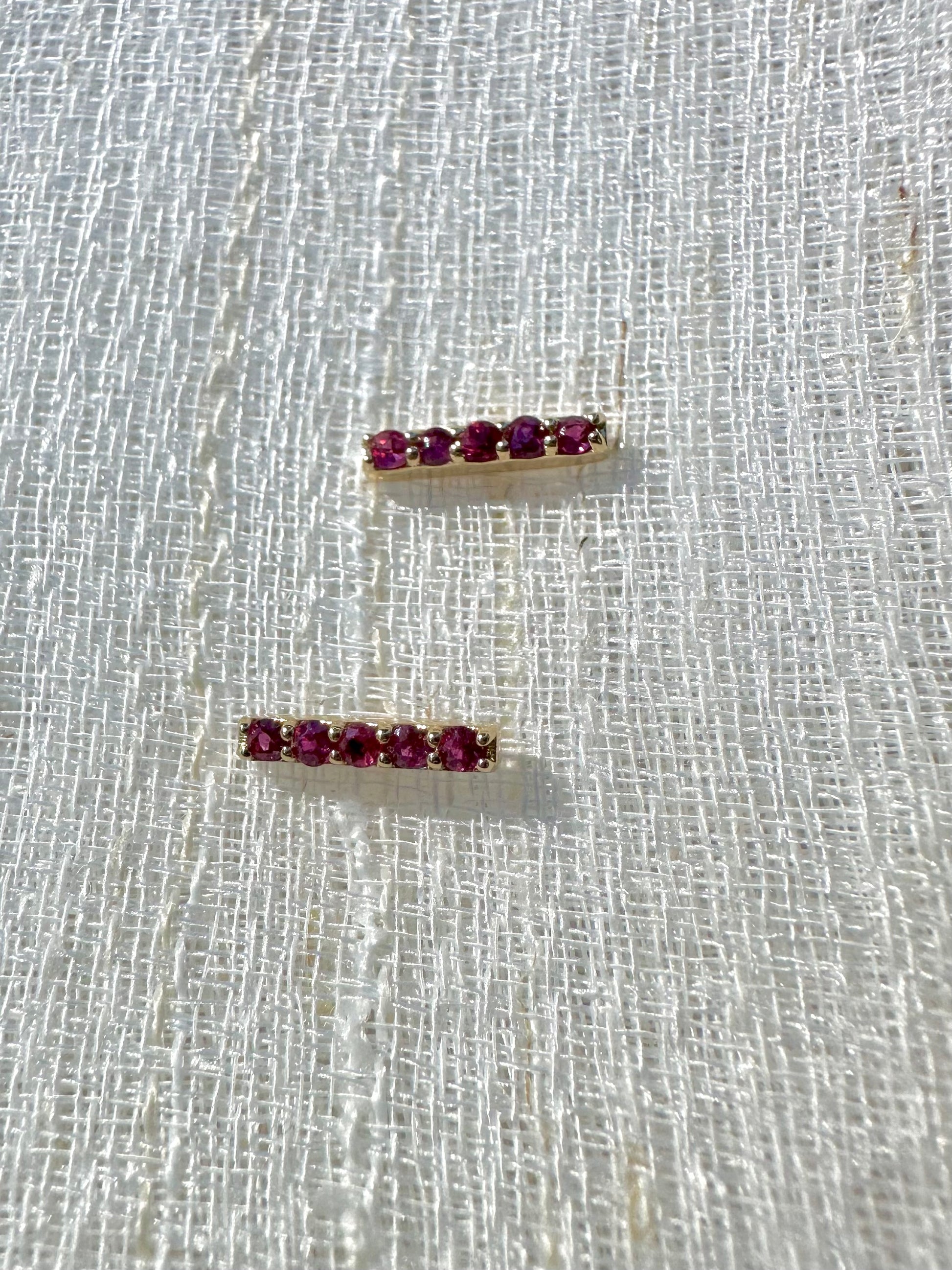 Beautiful and sleek Bar stud earrings adorned with 1.7mm round natural Ruby gemstones. Handcrafted in 18 karat Gold, these Ruby Stud Earrings have a linear design that makes them comfortable for everyday wear. Sold as pair.